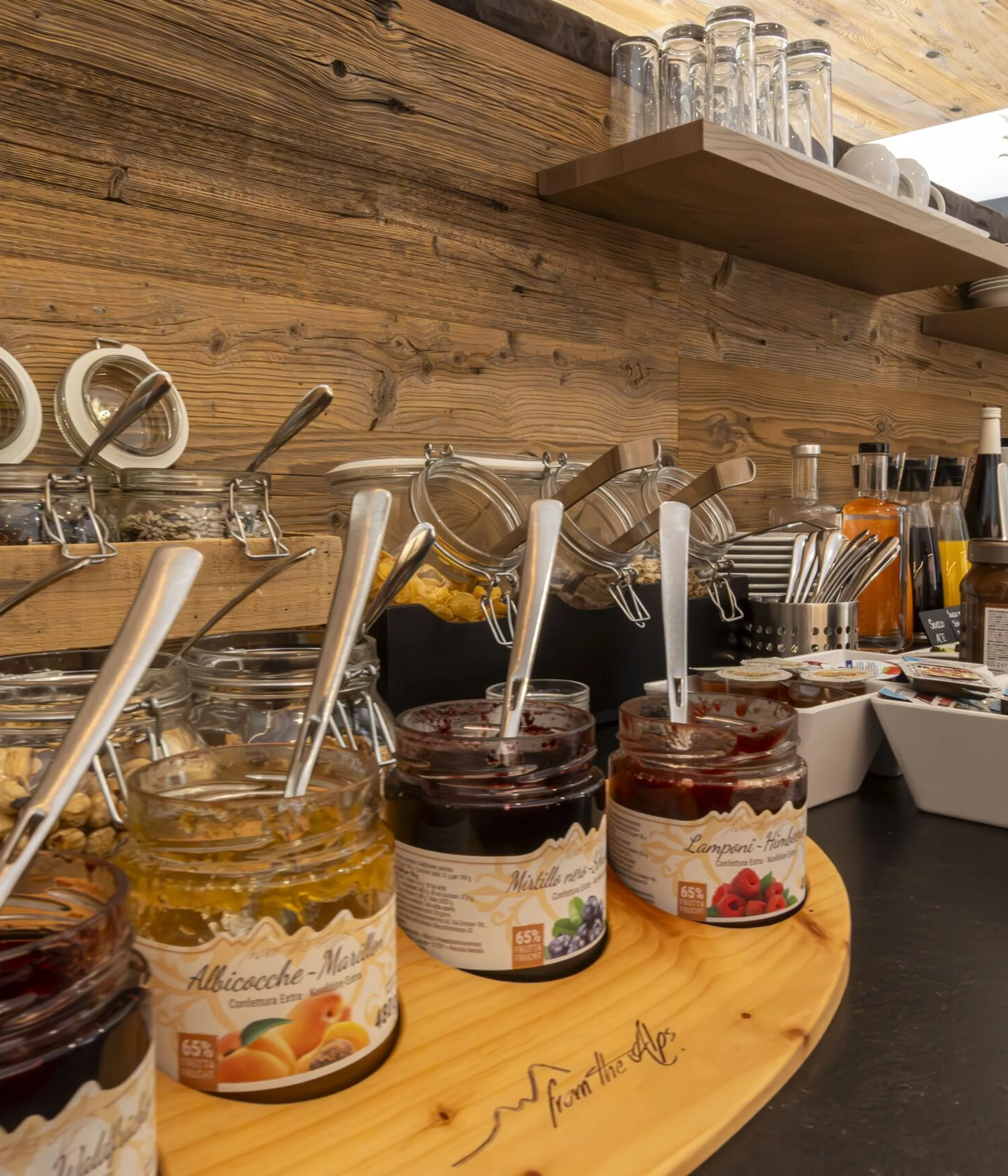 Assorted jams, nuts, and spreaders on a wooden buffet with jars, spoons, and shelves in a rustic cafe.